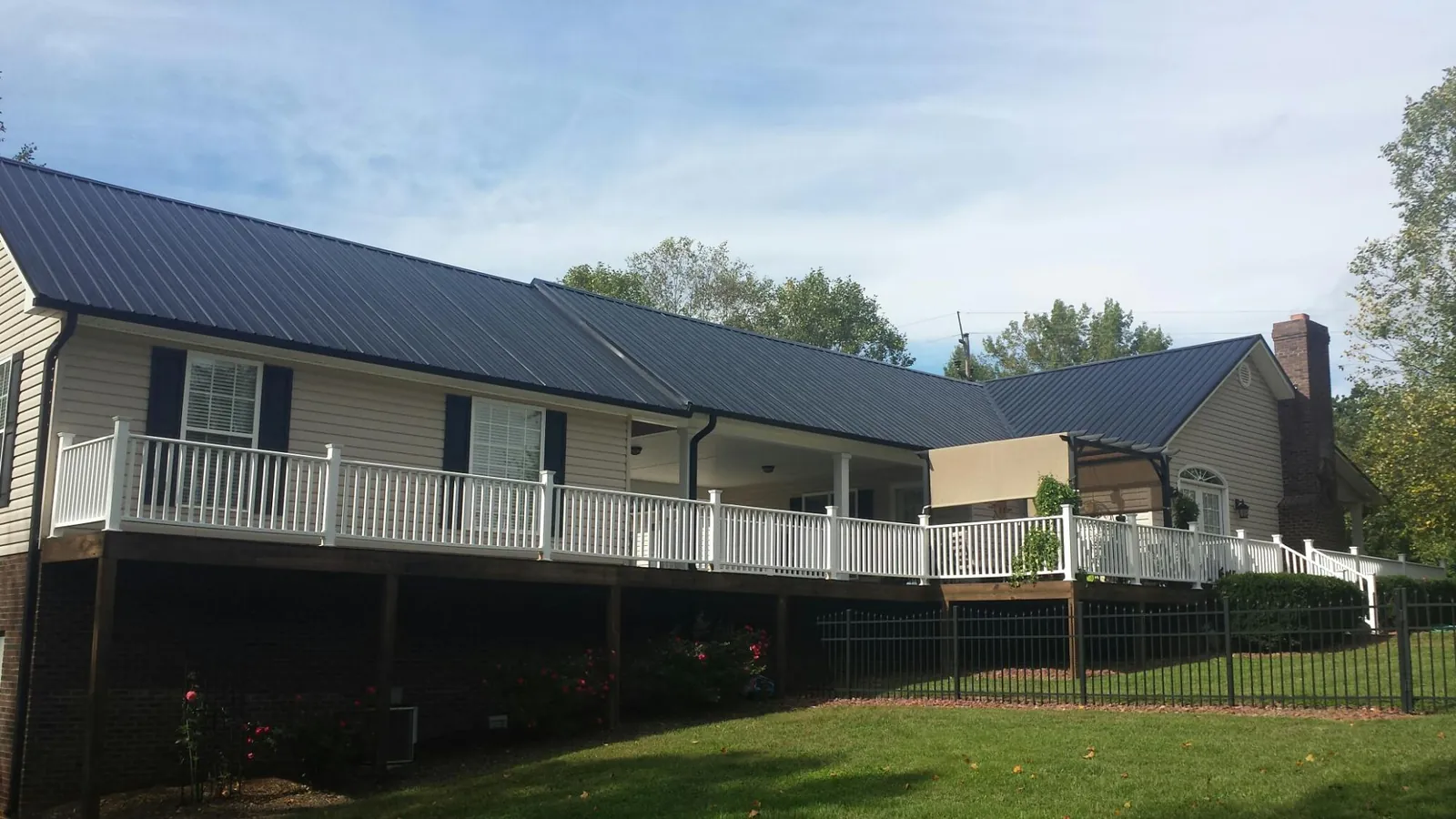Black metal roof above a long white railed deck on a hillside home in Monroeville